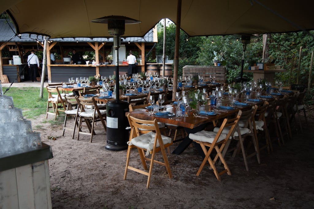 Lange tafels ingedekt voor diner voor trouwfeest onder stretchtent bij de open keuken