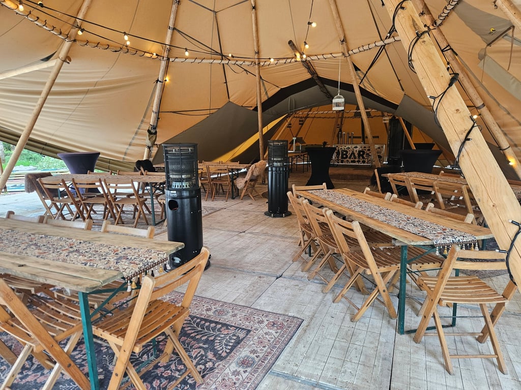 Overdekte eventlocatie met houten tafels, heaters, verlichting, eigen bar en unieke sfeer.  