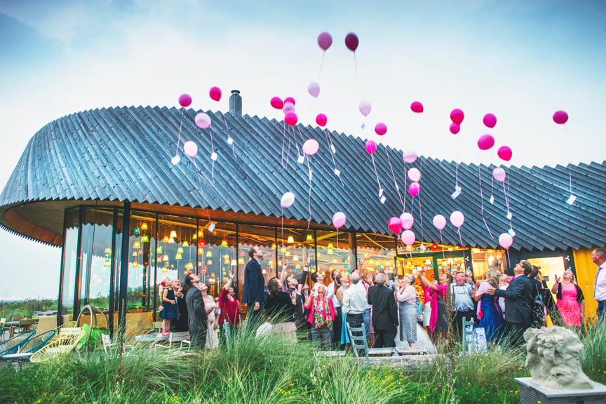 De locatie is te zien met gasten die ballonnen loslaten. Een feestelijk gezicht. Binnen branden de kleurrijke lampjes.