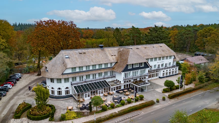 Hotel-Restaurant De Mallejan is een charmant landhuis in Engelse stijl, omringd door groen, met een statige witte gevel, een prachtig rieten dak en een klassieke, elegante uitstraling.